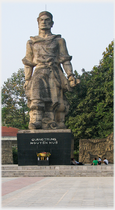 Styalised sixty foot statue, small group of people near base.