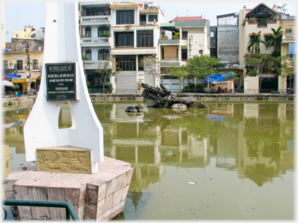 White support with plaque and small lake with metal debris beyond.