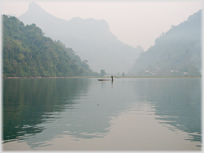 Lake with mountains and man standing on basic boat.