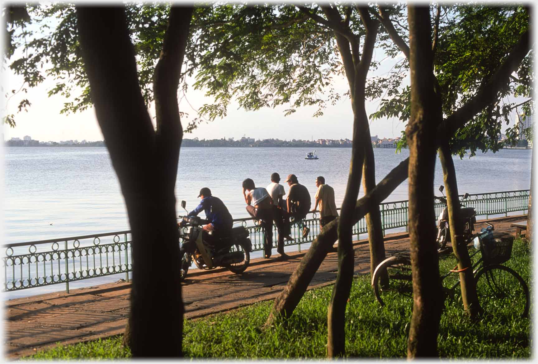 Group of men seen through trees by the lake.