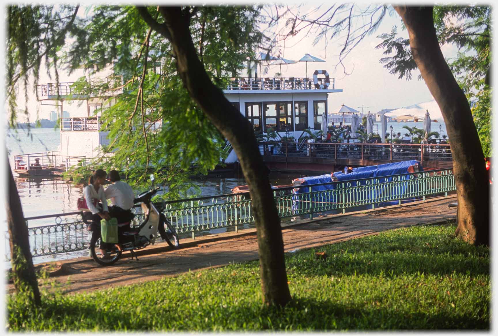 Moored restraunt boat, couple on motorbike by railings.