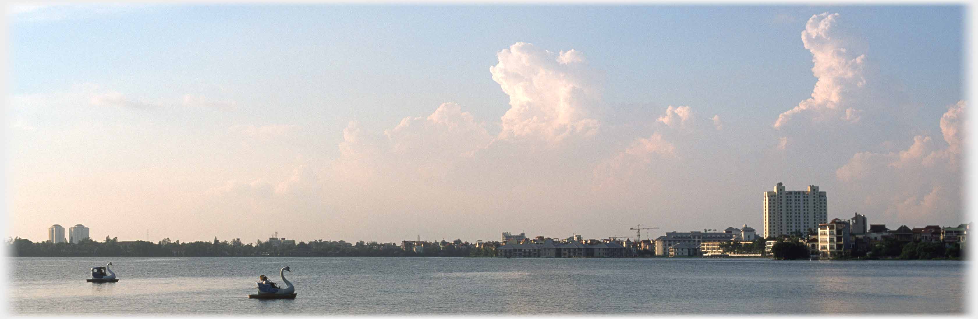 Far skyline of lake with two pedalos, towering cumulus clouds above.