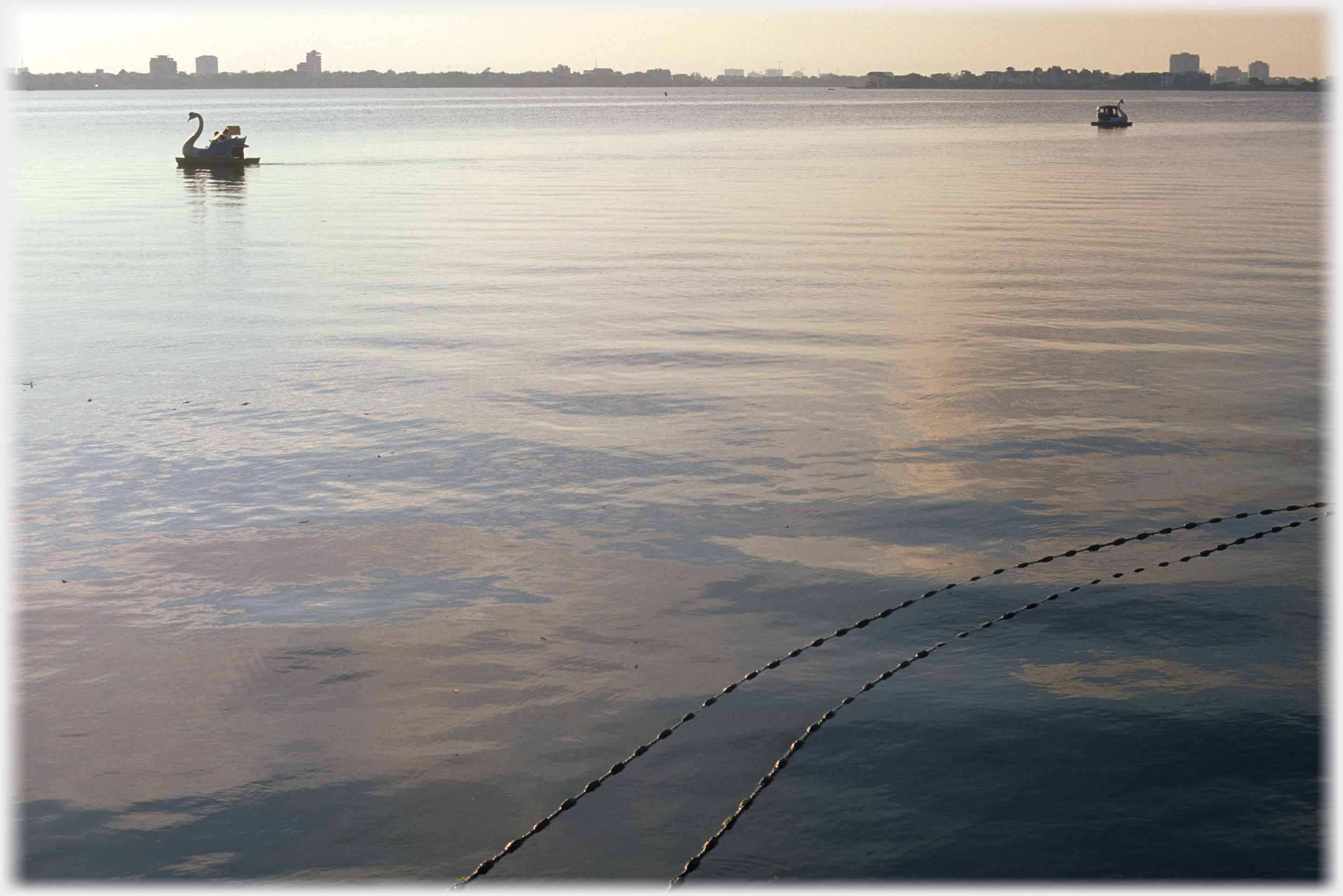 Two pedalos further off, floats at top of nets which hang in the lake, in the foreground.