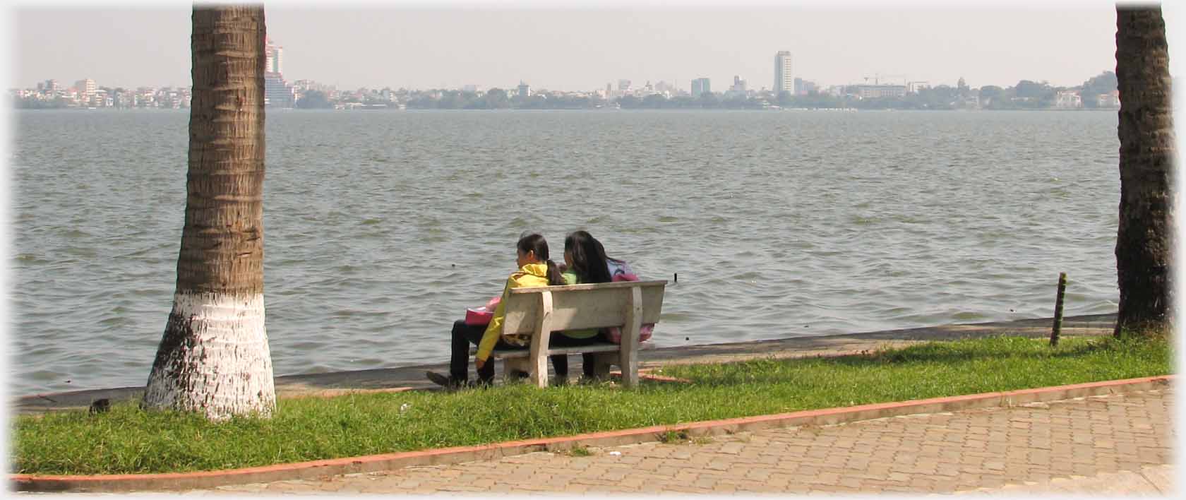Two younger girls on seat looking out across the lake towards city centre skyline.