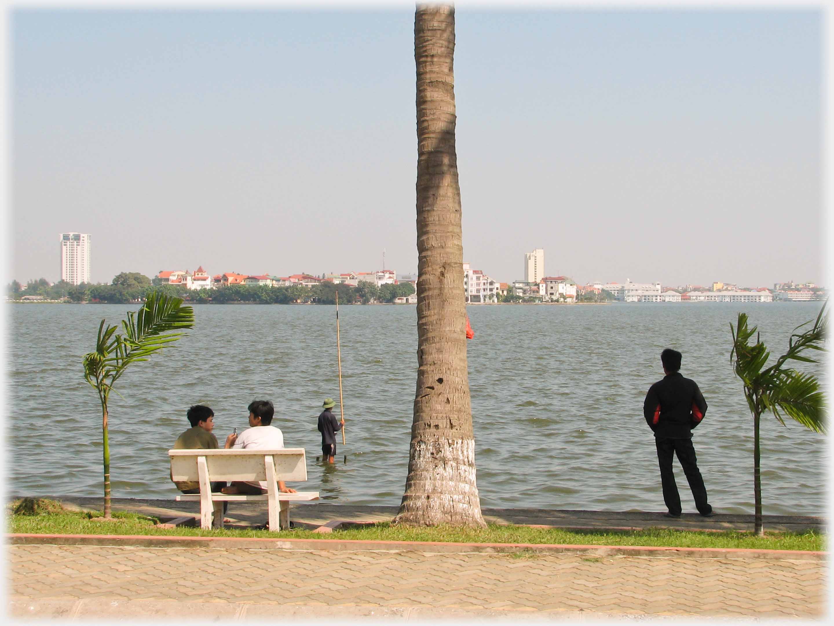 Shot with tree up centre, seat with two boys, fisherman and standing man.