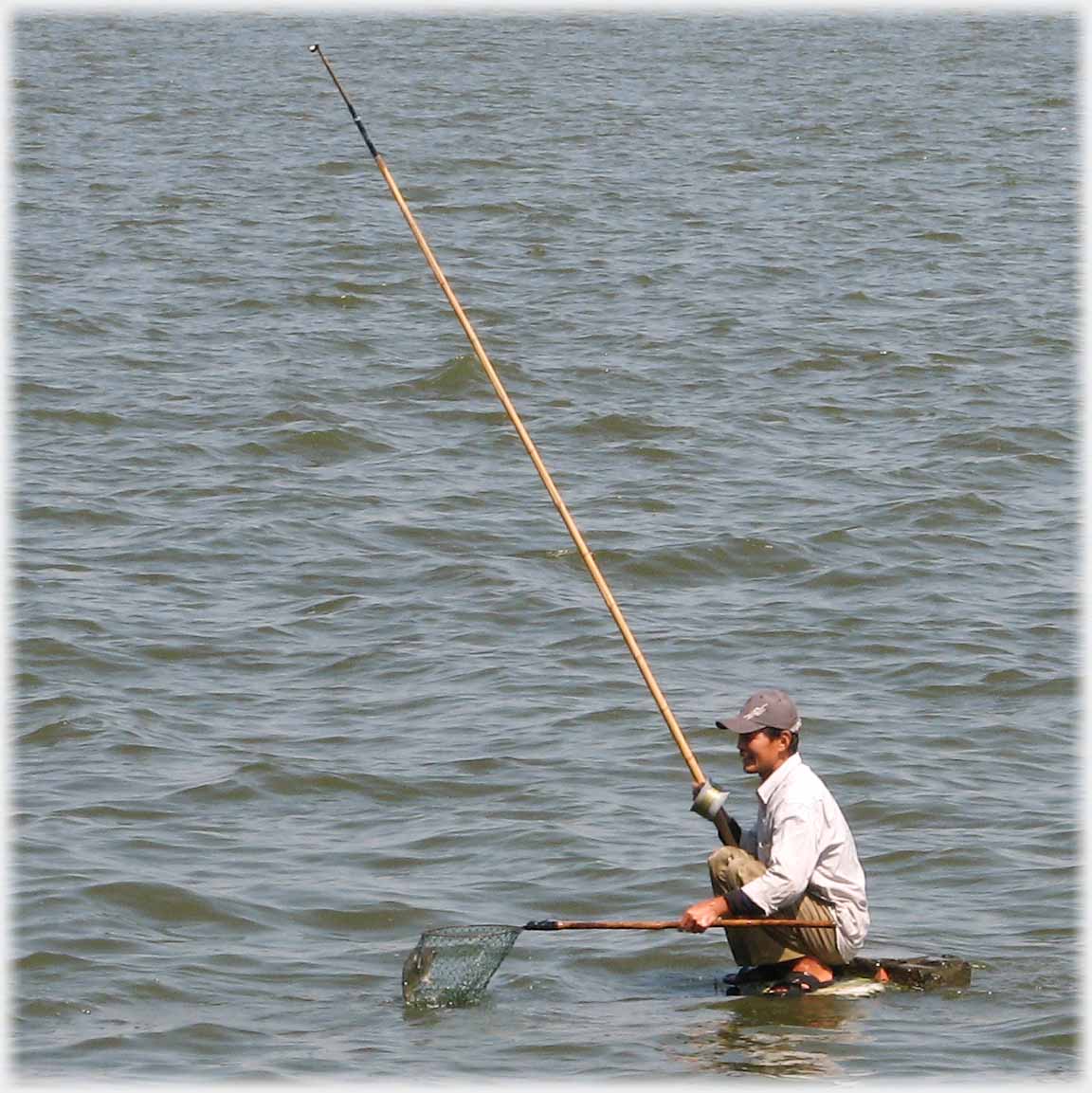 2 of 5 man squatting with net for fish.