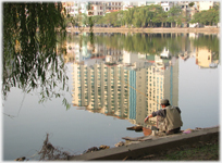 Man fishing into large reflection of hotel in lake.