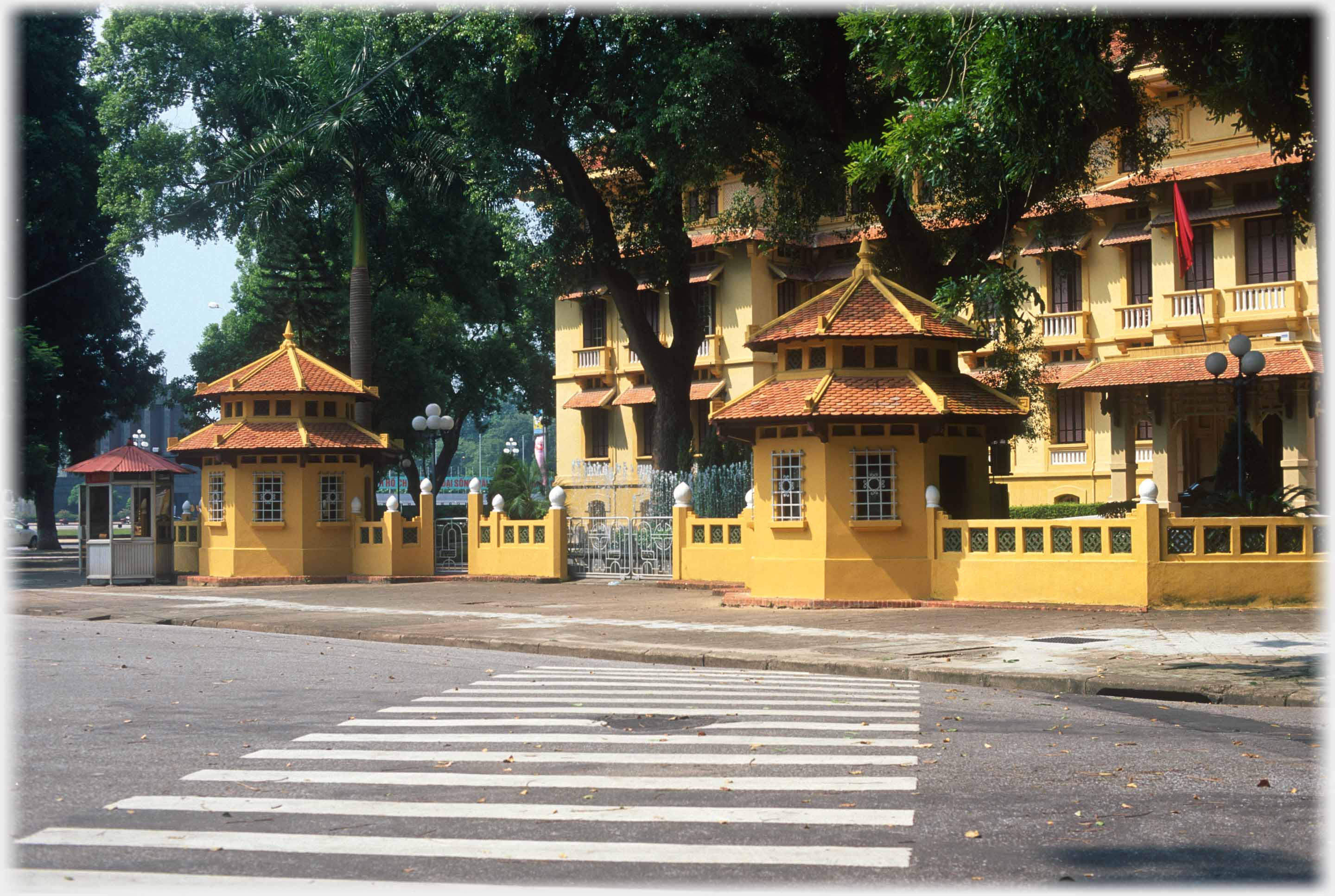 Two ochre gatehouses in front of similar coloured building wtih zebra crossing in foreground.