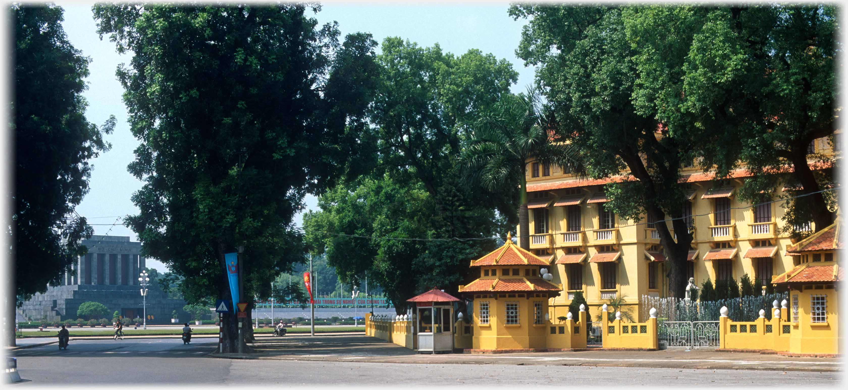 Same large building to right, trees and between them grey columned building in the distance.