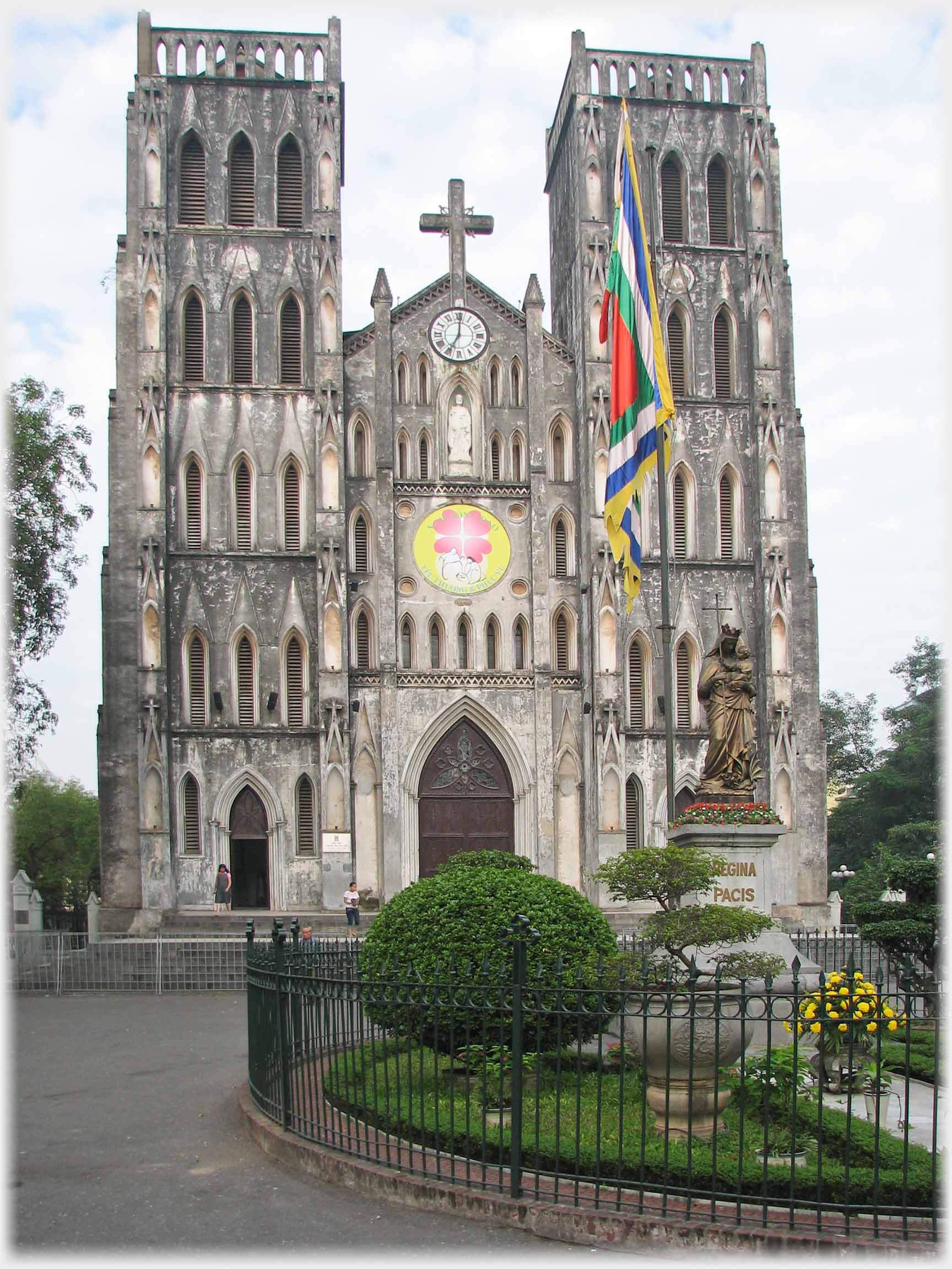 Facade of large church with flagpole and railed garden in front.