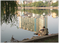 Man fishing into reflection of large building.