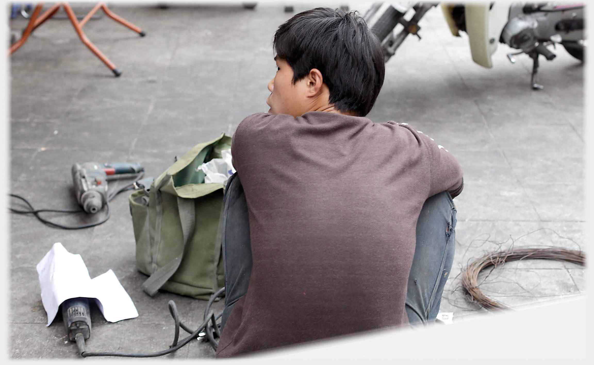 Man sitting on pavement with drill beside him.