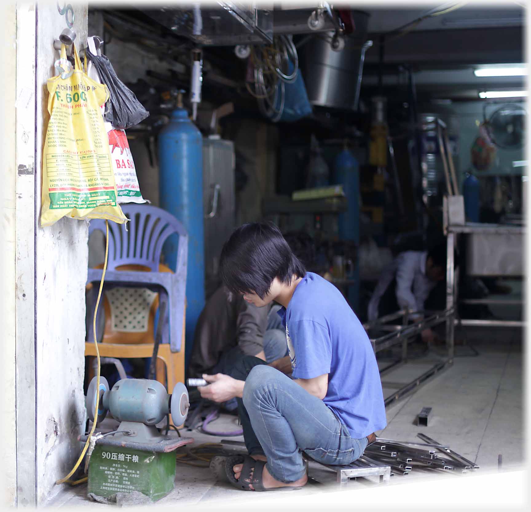 Man grinding metal on two disk grinder, other disk by electric cable.