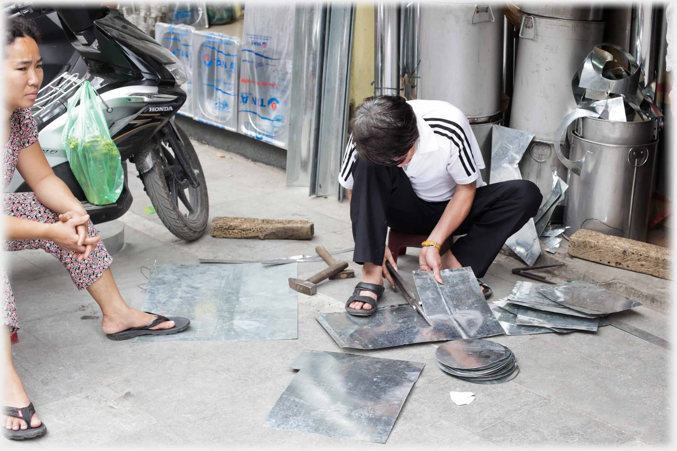 Man cutting metal woman sitting beside him.