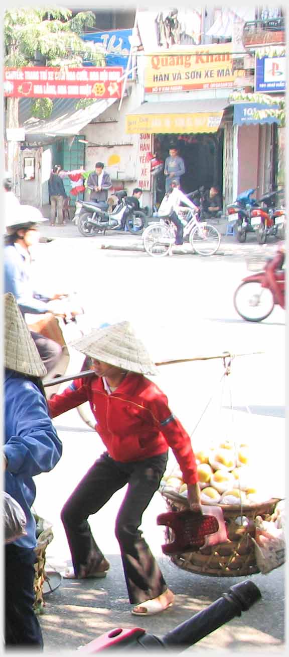 third of three shots of woman heaving heavy load of fruit off the ground - can see to be in the air.