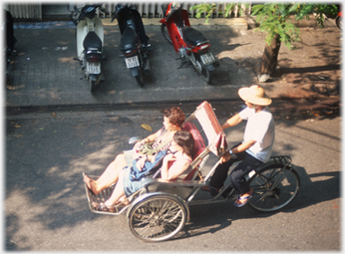 Man riding rickshaw with two women wearing domed hat.