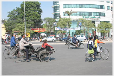 Older rickshaw in wide road with Viet woman in it.