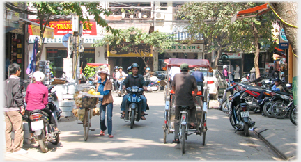 Street scene with hawker, motorcyclist and rickshaw.