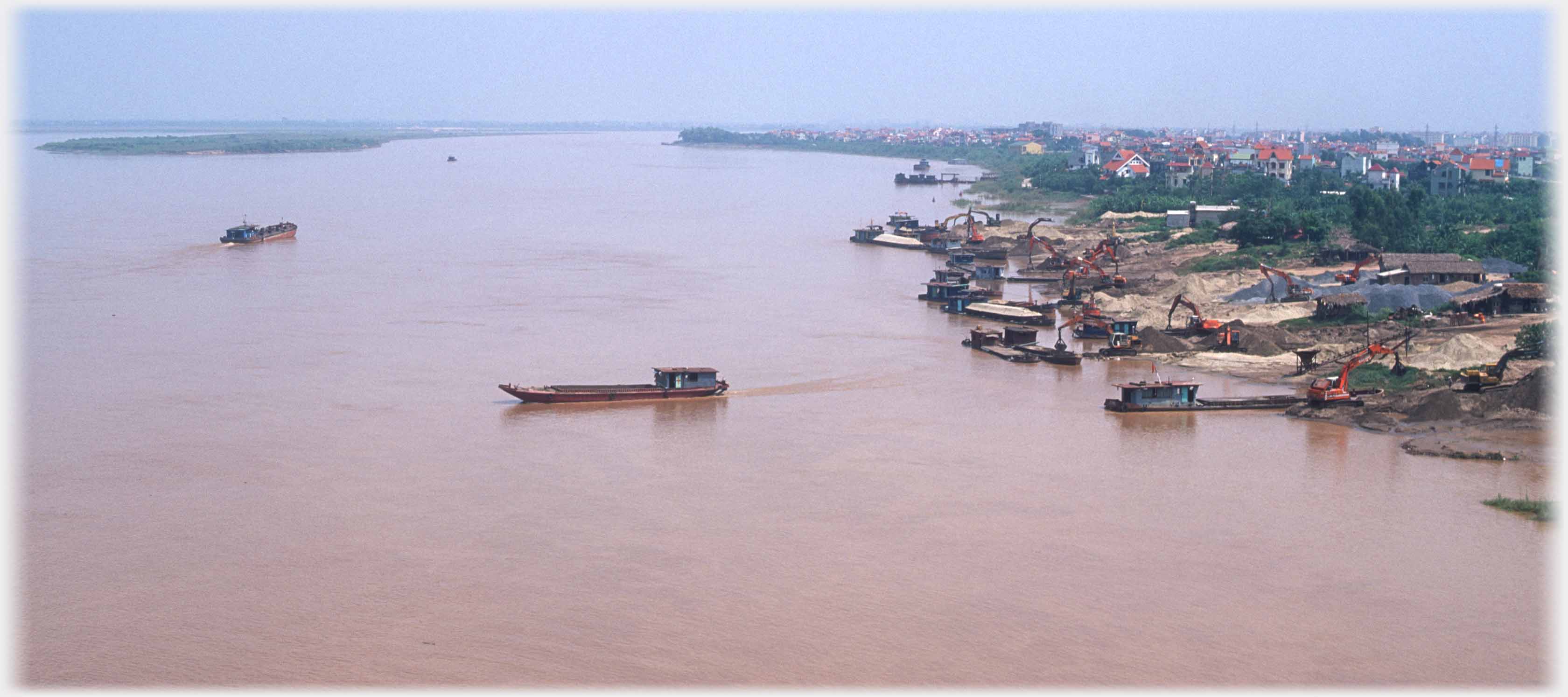 Two barges on wide river with diggers unloading at river bank on right.