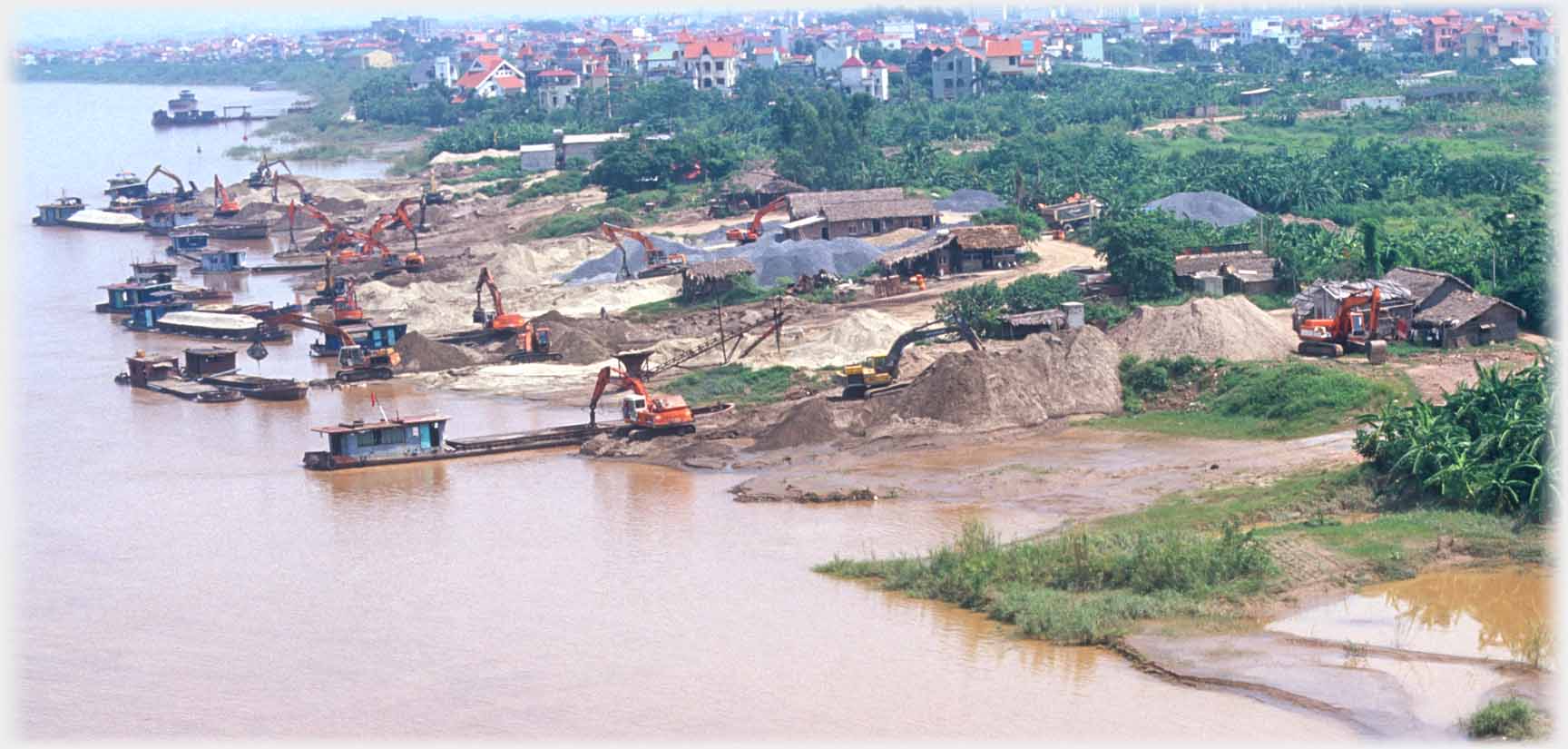 Diggers unloading silt from barges at river bank.