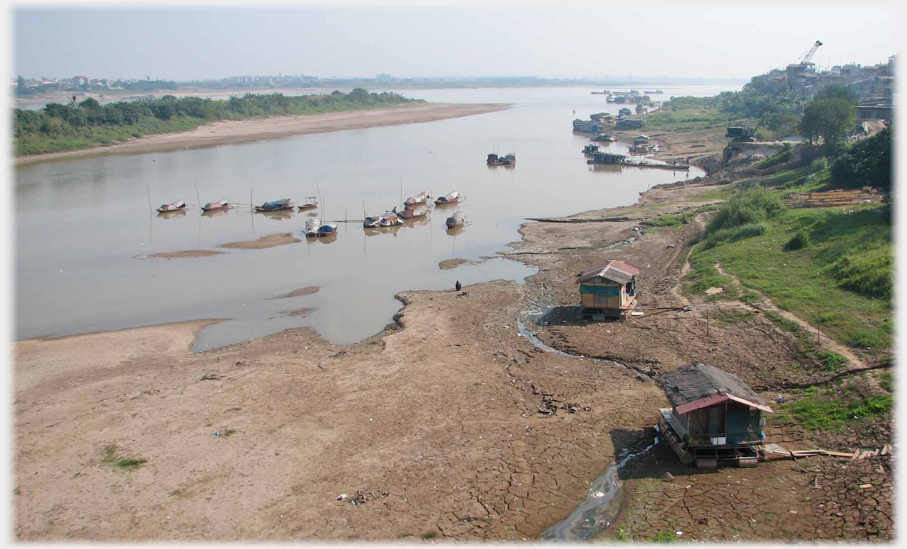 Overview of backwater opening to main river with mudflats and houseboats.