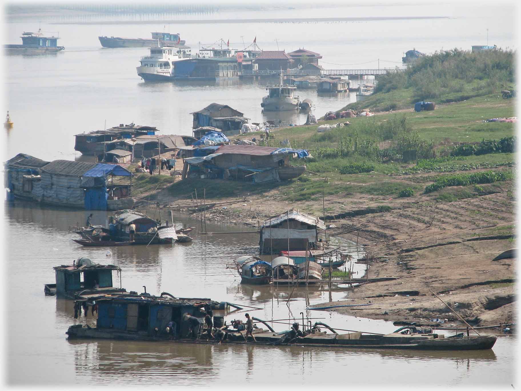 Various working boats at river bank on which signs of agriculture can be seen.