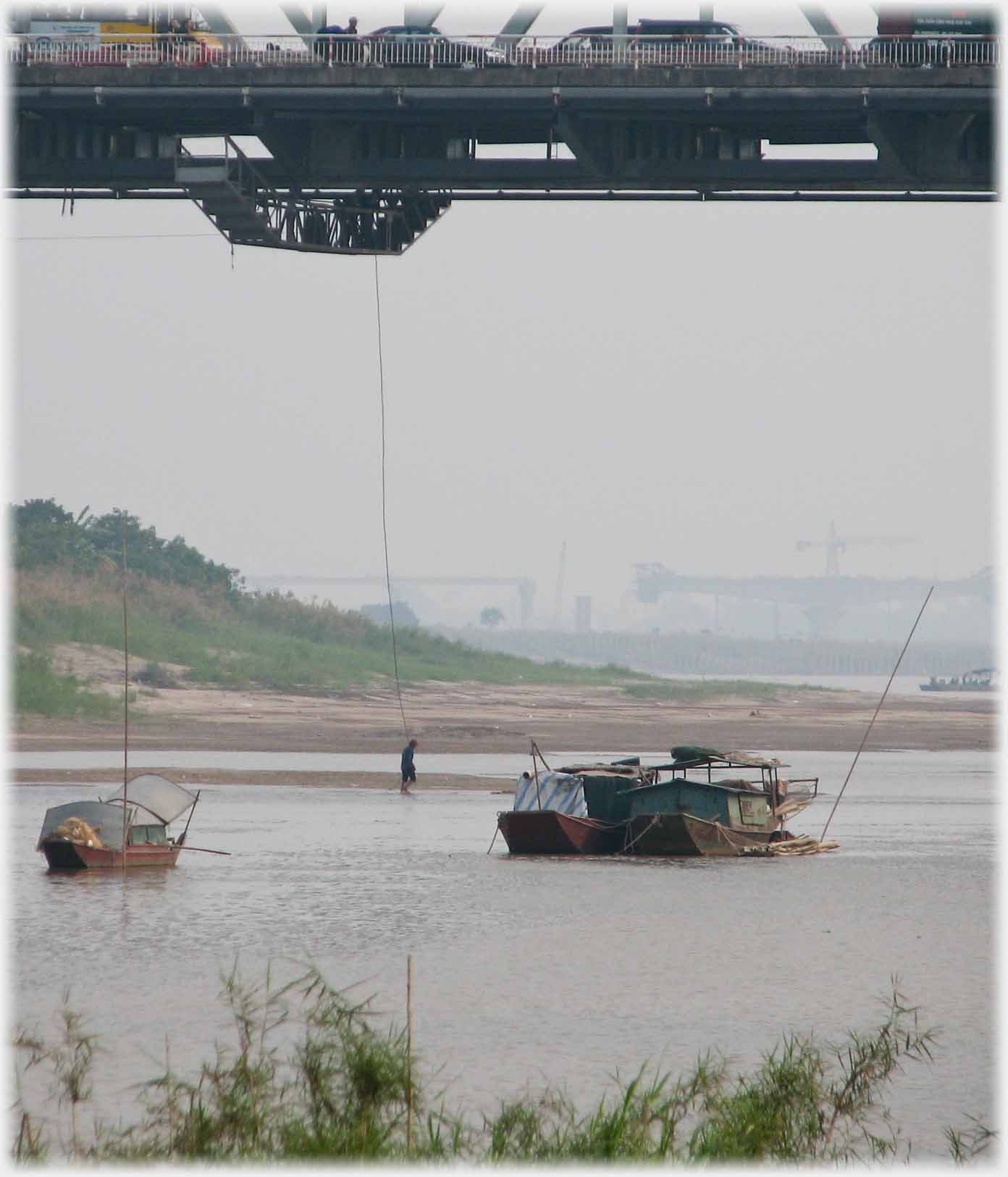 Man standing in water with rope from him to bridge above.