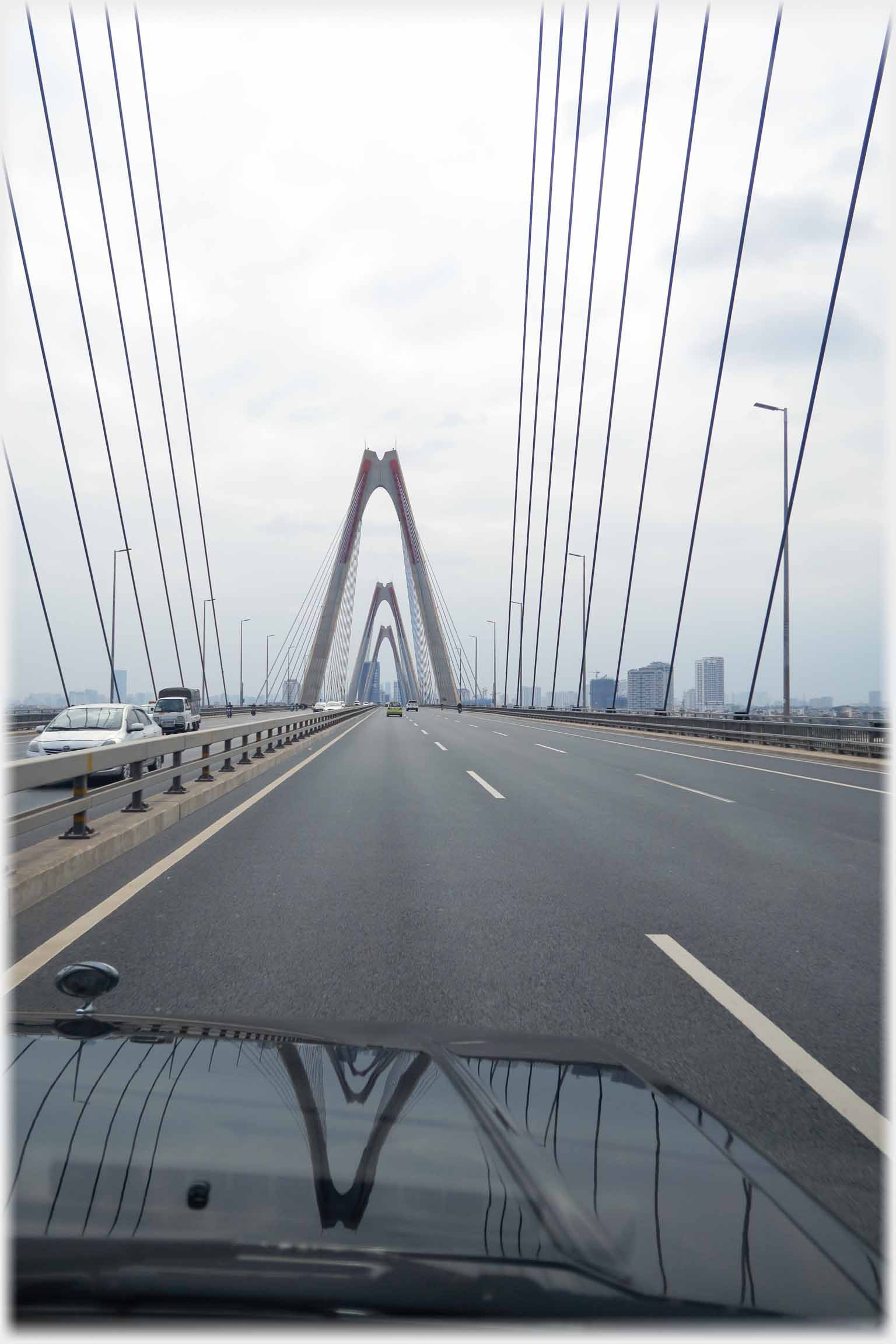 Bonnet of car with road in front and suspension bridge arches and cables.