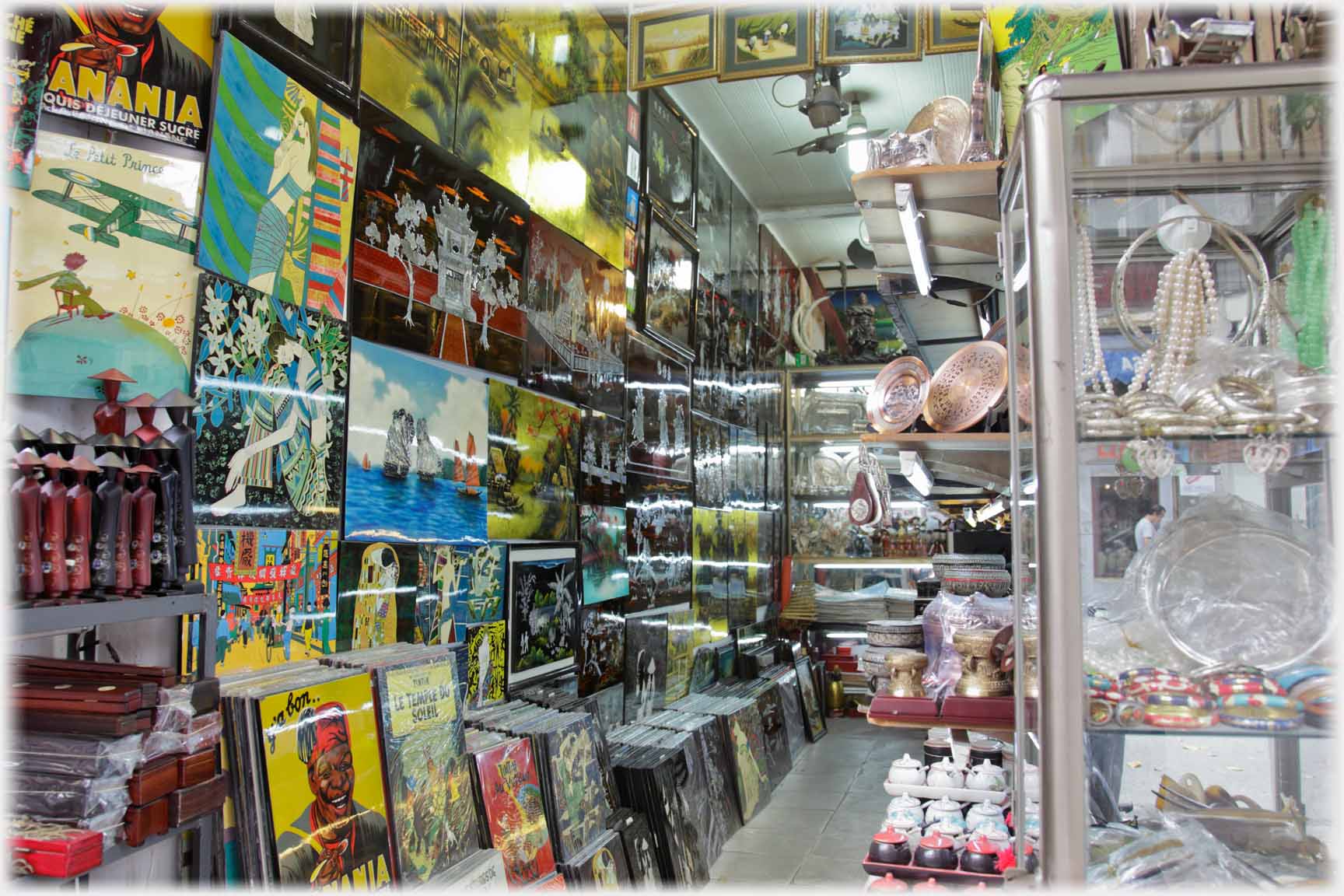 Another shop full of paintings with jewelry cabinet in foreground.