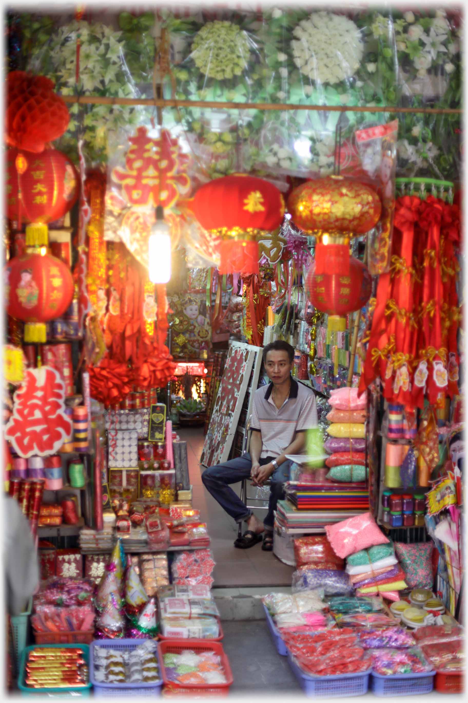 Man sitting totally surrounded by red lamps and decorations.