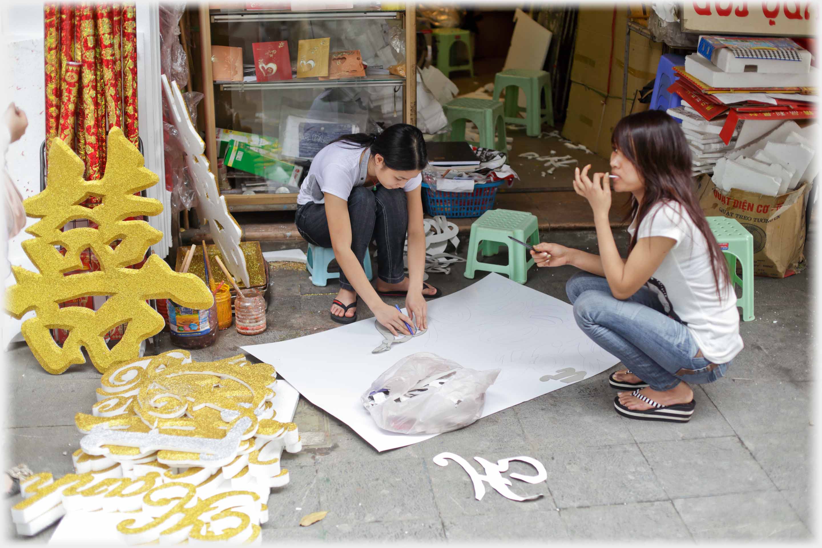 Two women squatting preparing a sheet of paper.