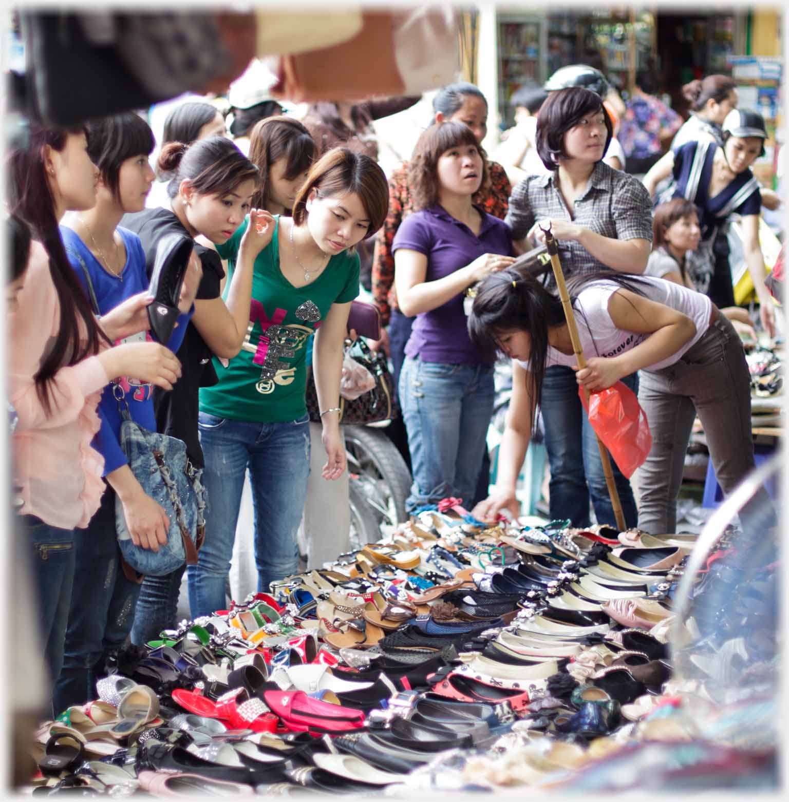 Women crowding to look at shoes laid out in front of a shop.