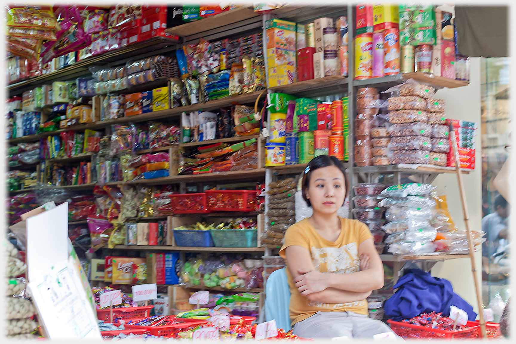 Woman with an air of abstraction in front of piled shelves of sweets.