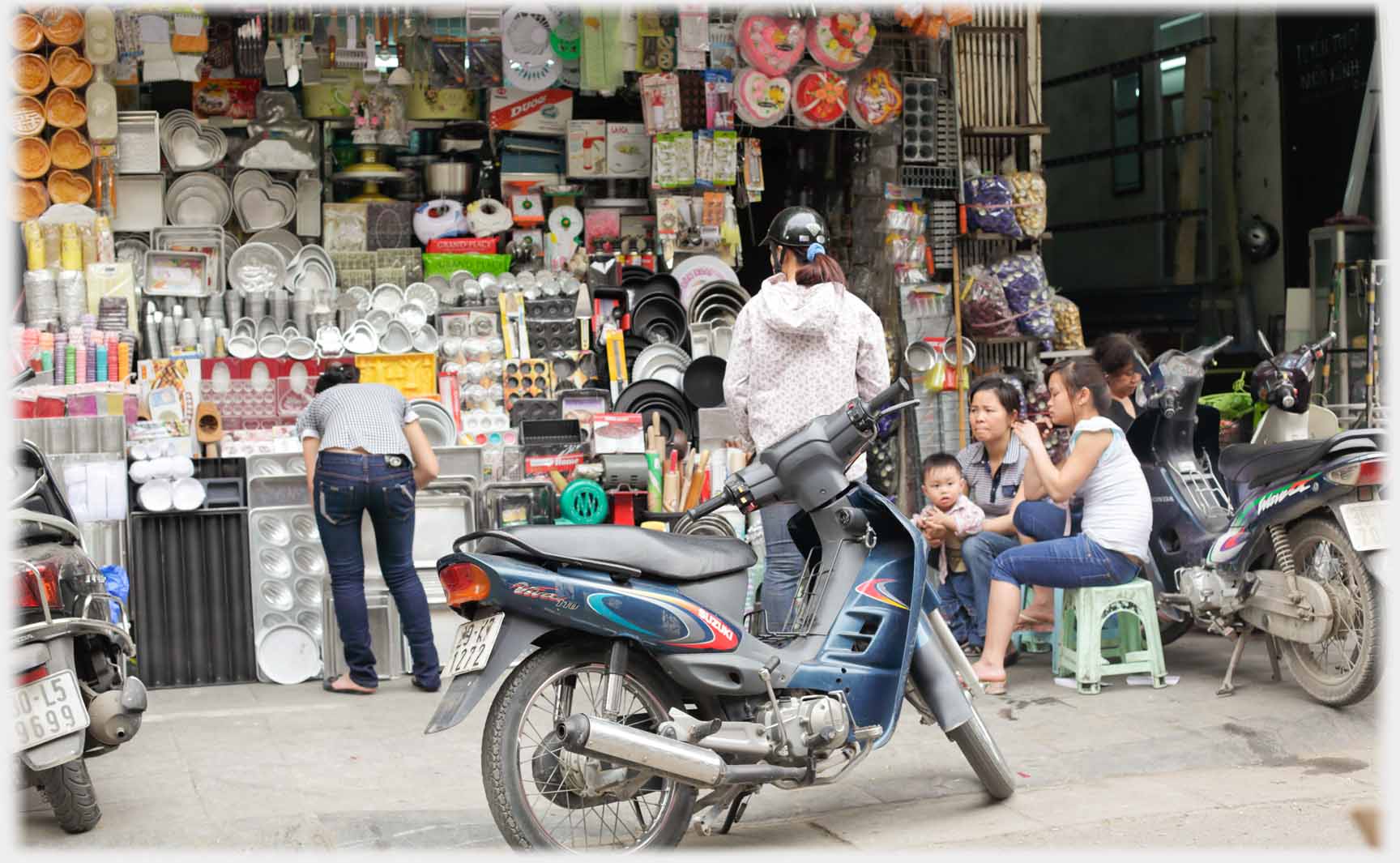 Family sitting by shop with motorbike parked in front.