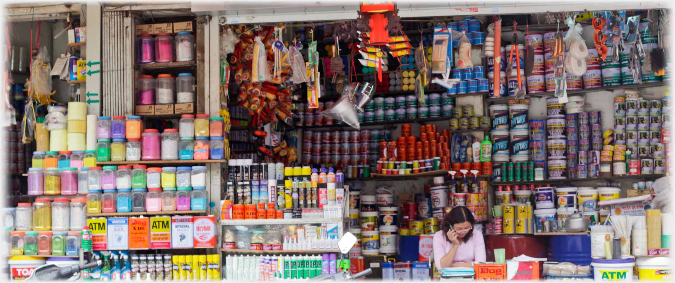 Woman talking on phone  with many shelves of paints and dyes behind her.