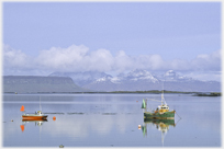 Two boats on calm sea, mountains beyond.