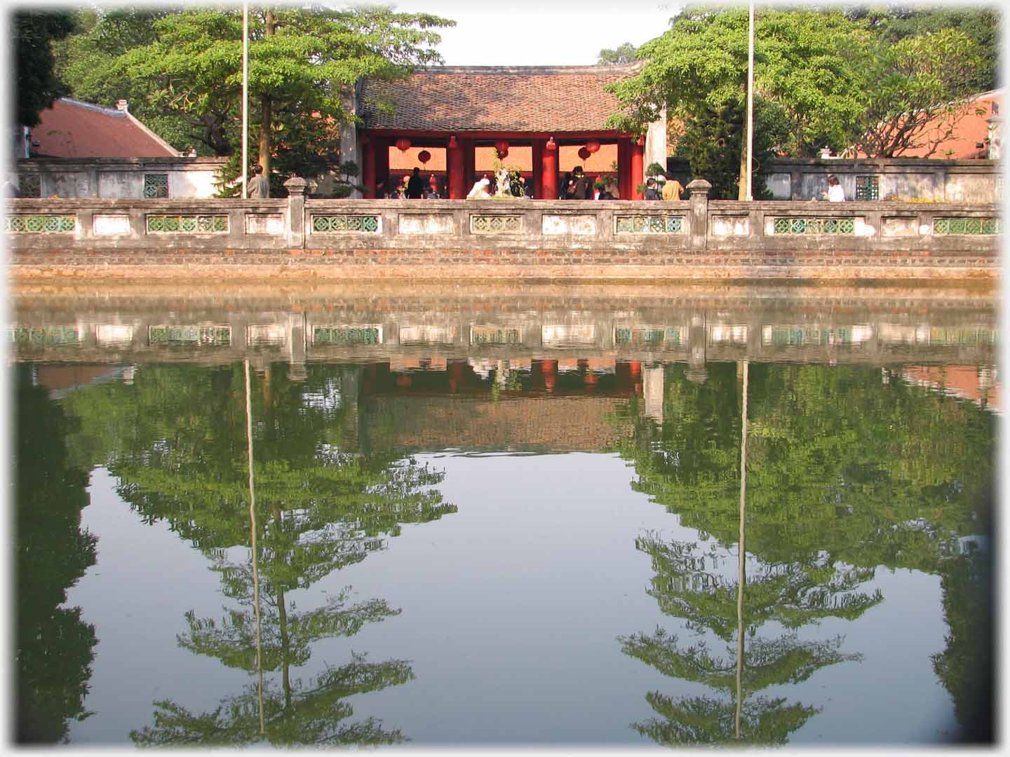 Small lake with reflections of trees, beyond small pavilion.