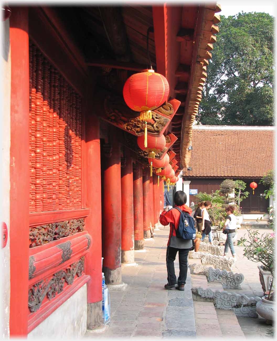 Looking close to and along red pillars of large pavilion with red lanterns and woman in red jacket.
