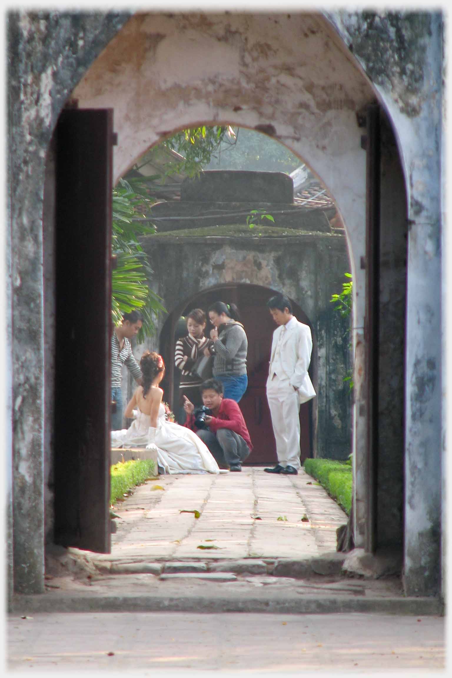 Looking through arch at wedding couple and their photographer.