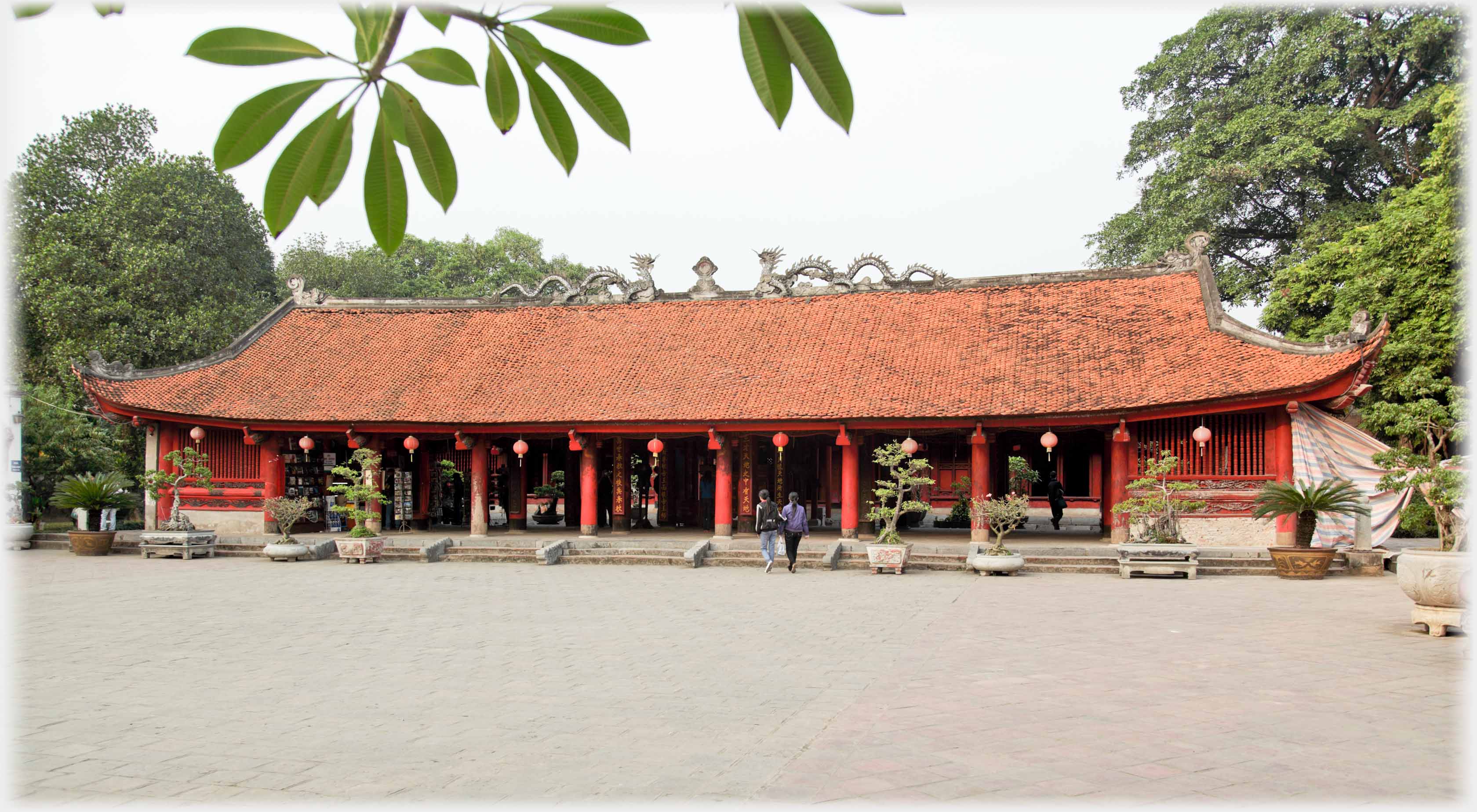 Long single story pavilion with red pillars and decorated roof.