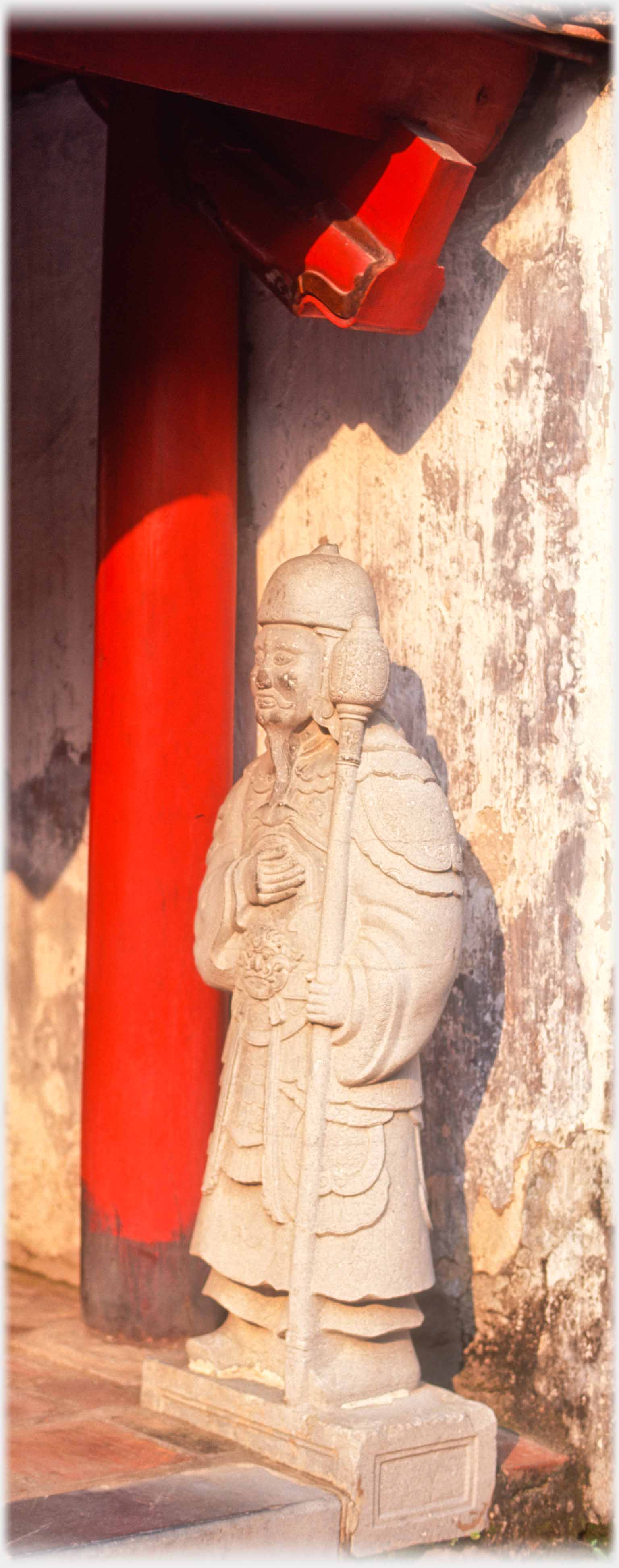 Stone figure in elaborate clothes holding mace.