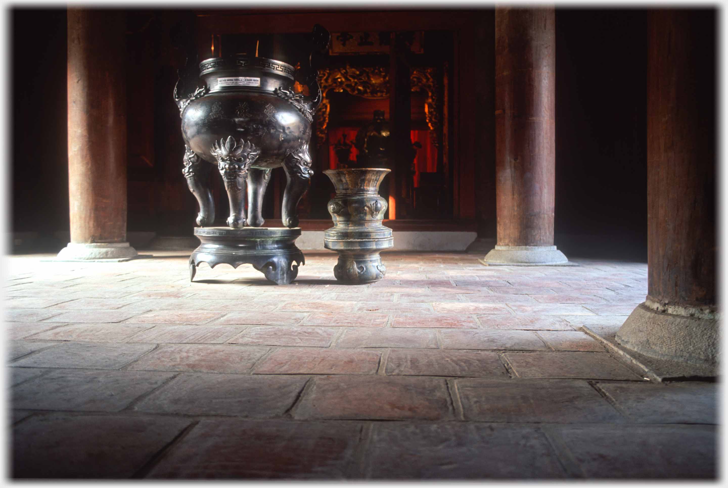Large urn with small one beside it on floor between pillars, inner room just visible.