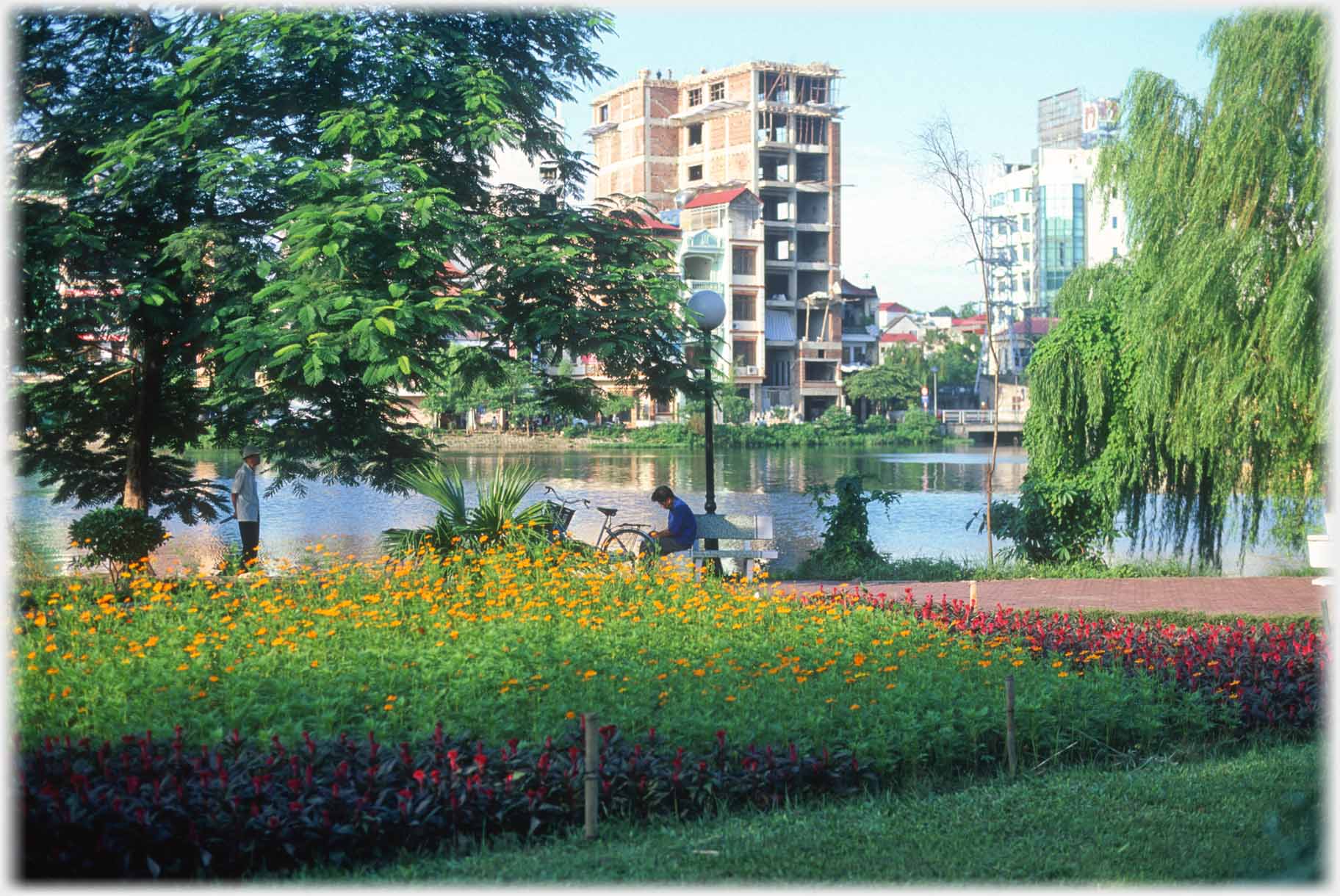 Man on seat and one standing, new building across lake.