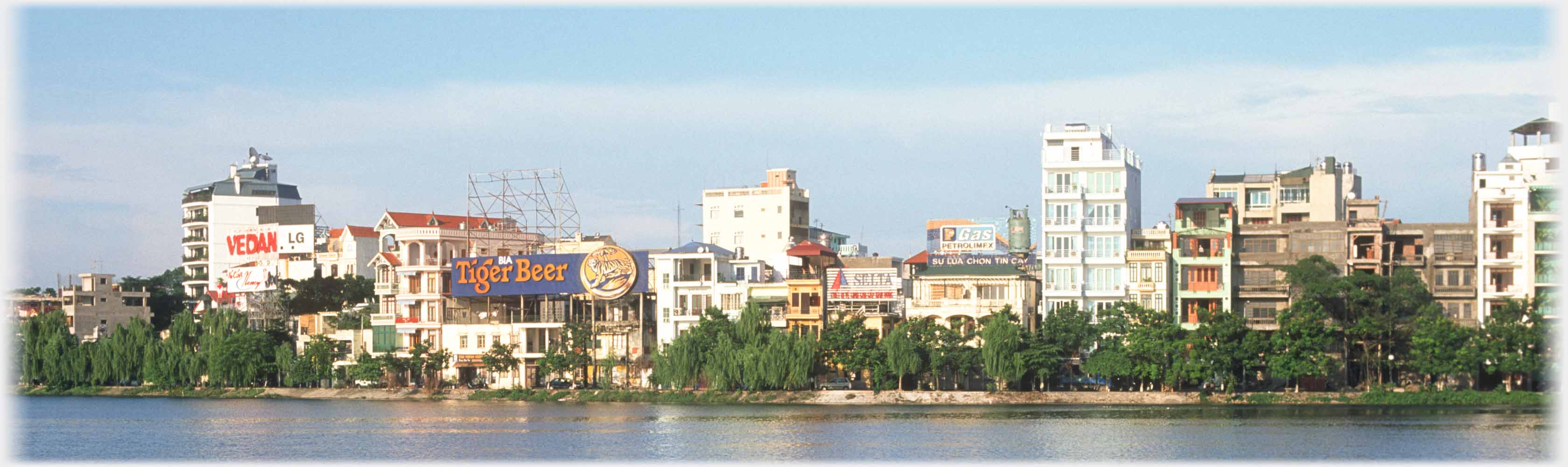 Shore line of blocks of flats behind trees, large Tiger Beer sign.