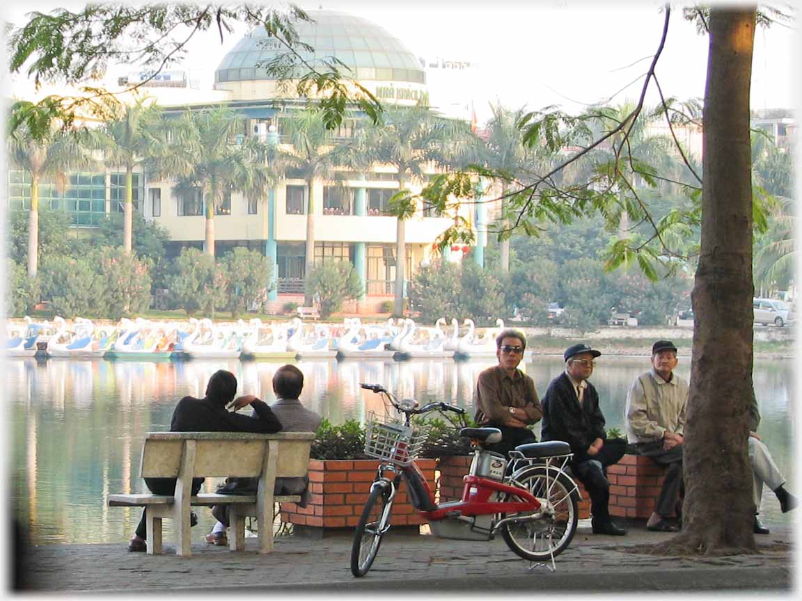 Men sitting on large planter display boxes looking at traffic and photographer, electric bike in front.
