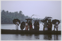 Line of people standing in boat in heavy rain with umbrellas.
