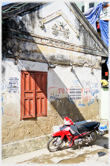 End wall of house with shuttered window and dated 1982, motorbike in front.