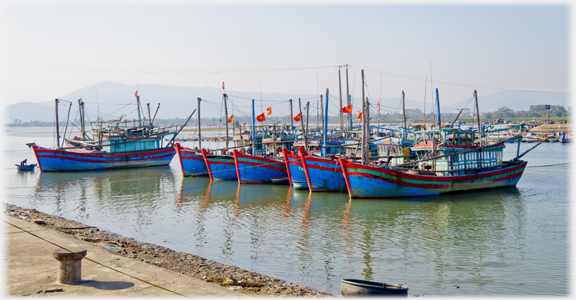 Quay with seven fishing boats and hill beyond.