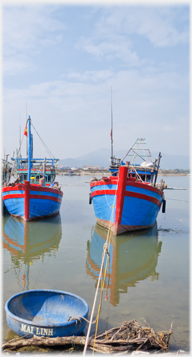 Two fishing boats out from the water's edge with a coracle by the bank.