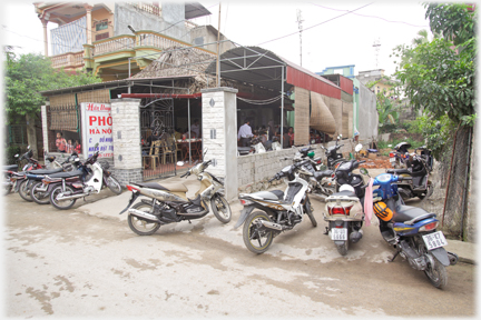 Customers motorbikes parked at entrance and beside cafe.